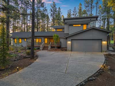 Charming mountain-style exterior with attached garage, curved driveway, and updated landscaping in the prestigious Forest Highlands community. Surrounded by pine trees, this Flagstaff luxury property blends elegance with natural beauty.