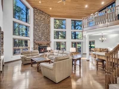 Spacious great room with dramatic vaulted wood ceilings, stone fireplace, and oversized windows framing peaceful golf course views. Designed for entertaining and relaxation, this luxury living area captures the essence of mountain living.