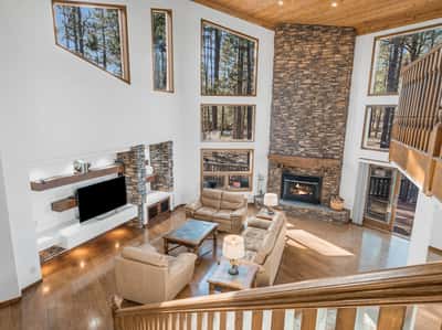 Elegant open-concept living area with soaring ceilings, rich wood flooring, and stunning stone fireplace centerpiece. Expansive windows flood the space with natural light while showcasing beautiful Forest Highlands scenery.