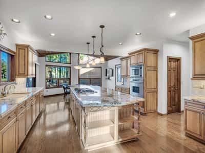 Expansive chef-inspired kitchen with large center island, granite surfaces, premium appliances, walk-in pantry, and abundant storage. Oversized windows and warm wood finishes create a welcoming atmosphere with scenic golf course views.