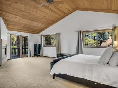 Elegant primary bedroom with fireplace, private deck access, and serene views of the Canyon Golf Course. Warm wood finishes and oversized windows create a relaxing retreat surrounded by towering pines.