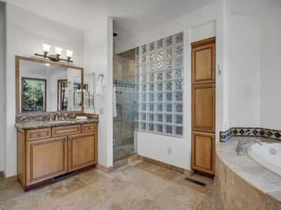 Spacious ensuite bathroom featuring glass block shower details, custom cabinetry, and elegant tilework throughout. Designed for everyday luxury, this primary bath combines comfort with timeless mountain-inspired finishes.
