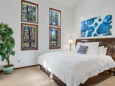 Bright and inviting guest bedroom with large windows, plush carpeting, and scenic pine tree views. This comfortable secondary suite offers a quiet retreat perfect for visitors or full-time living in Forest Highlands.