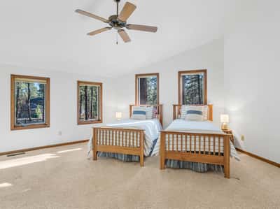 Spacious guest bedroom featuring vaulted ceilings, large windows, and tranquil forest scenery. Perfect for hosting family and friends, this inviting space reflects the relaxed luxury of Forest Highlands living.