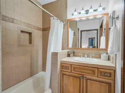 Clean and elegant bathroom with custom wood cabinetry, tiled shower and tub combination, and warm natural finishes. This well-designed guest bath adds functionality and comfort to the home s spacious floor plan.