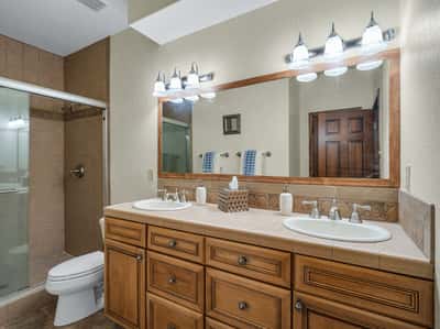 Well-designed guest bathroom featuring dual vanities, tiled finishes, custom cabinetry, and bright lighting. This spacious bath provides comfort and functionality for family and overnight guests.