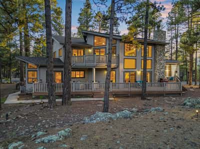 Impressive exterior featuring expansive decks, dramatic architecture, and large picture windows surrounded by towering pines. This Forest Highlands residence blends luxury living with the natural beauty of Flagstaff.