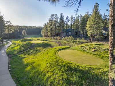 Scenic views of the 13th hole surrounded by rolling greens, walking paths, and towering pine forests. This peaceful golf course environment offers a relaxing mountain lifestyle in Flagstaff.