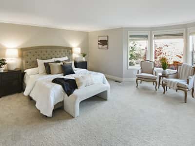 Spacious bedroom features large windows and cozy seating, perfect for relaxation and natural light.