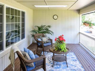 Spacious covered porch featuring cozy seating, vibrant plants, and ample natural light for gatherings.