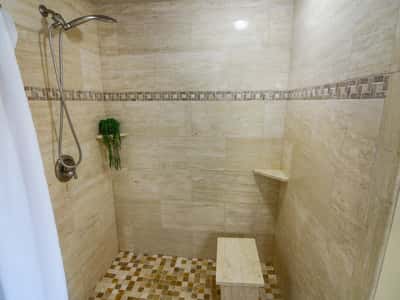 Experience a modern shower space featuring natural stone finishes, a built-in bench, and open design.