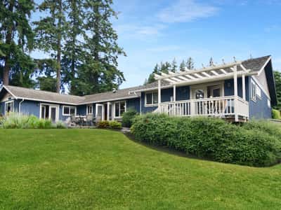 Sprawling blue home with expansive green lawn, surrounded by trees and ideal for outdoor entertaining.