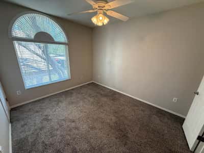 Inviting bedroom with a large arched window, ceiling fan, plush carpeting, and natural light. This versatile room in Phoenix provides excellent flexibility for guests, work, or everyday living.