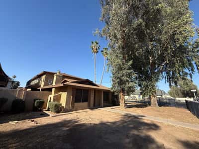 Front exterior view featuring mature trees, covered entry, and desert-inspired landscaping. This inviting Phoenix property combines comfort, convenience, and established neighborhood appeal.