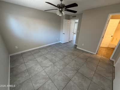 Spacious bedroom featuring tile flooring, ceiling fan, neutral finishes, and convenient access to the bathroom. The flexible layout offers a comfortable and relaxing retreat at the end of the day.
