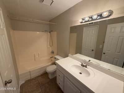 Well-maintained bathroom showcasing a large vanity, oversized mirror, tub and shower combination, and abundant lighting. Functional design and easy-care finishes enhance everyday convenience.