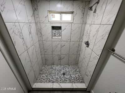 This impressive walk-in shower highlights oversized marble-look tile, a built-in niche for convenience, and stylish finishes throughout. The updated design creates a luxurious feel within this remodeled Phoenix residence.