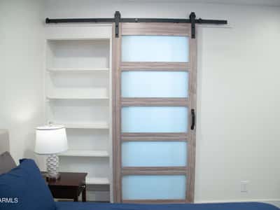 A contemporary sliding barn door and built-in shelving create both style and functionality within the primary bedroom. These custom touches enhance the remodeled interior and modern aesthetic throughout the home.