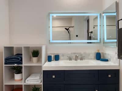 This updated bathroom showcases a sleek vanity, generous storage, illuminated mirrors, and modern finishes. The thoughtful remodel delivers both convenience and contemporary design.