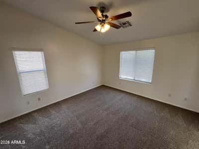 Bright secondary bedroom with plush carpeting, ceiling fan, and large windows that fill the room with natural light. Perfect for guests, family members, or a home office setup.