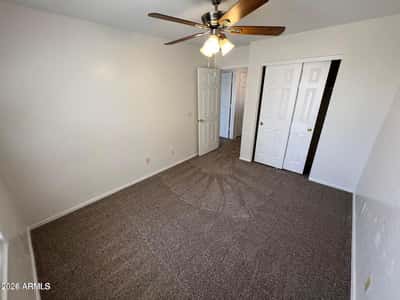 Bright guest bedroom showcasing fresh carpeting, neutral finishes, ceiling fan, and ample closet space. The functional layout makes this room ideal for visitors, family members, or a dedicated workspace.