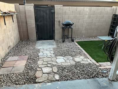 Fenced backyard features decorative rock landscaping, artificial turf, and a covered patio, creating an easy-care outdoor retreat ideal for entertaining or relaxing.