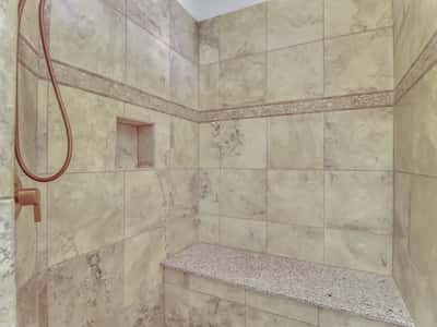 Relax in the beautifully finished walk-in shower featuring full-height tile, decorative accents, a built-in bench, and recessed storage niche. A spa-inspired feature that enhances this Glendale residence.