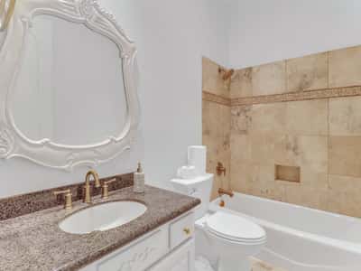Featuring a granite vanity, elegant fixtures, decorative framed mirror, and tiled tub and shower surround, this full bathroom blends functionality with timeless design in this Glendale property.
