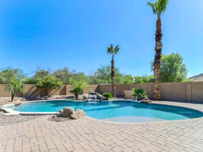 Resort-inspired backyard with a freeform swimming pool, rock waterfall, paver patio, palm trees, and beautifully landscaped grounds providing a relaxing outdoor escape in Glendale.