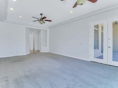 Elegant primary bedroom featuring French doors to the covered patio, tray ceiling, dual ceiling fans, plush carpeting, and abundant natural light. This Glendale home offers a relaxing private retreat.