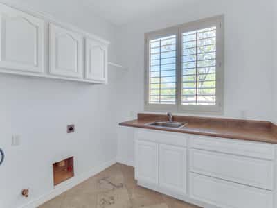 Well-equipped laundry room featuring built-in cabinetry, utility sink, countertop workspace, plantation shutters, and durable tile flooring. This Glendale residence provides excellent organization and everyday functionality.