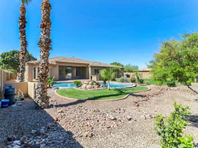 Resort-inspired backyard showcasing a sparkling pool, rock waterfall, mature trees, lush lawn, and covered patio. This Glendale property provides exceptional outdoor living and entertaining opportunities.