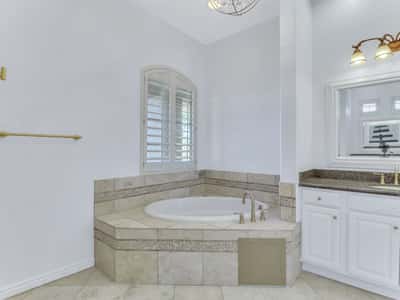 The primary bathroom features a spacious soaking tub with tiled surround, granite vanity, plantation shutters, and elegant finishes, providing a relaxing spa-inspired experience in this Glendale home.