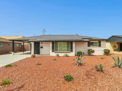 Front exterior showcasing attractive desert landscaping, updated paint, covered entry, and rooftop solar panels that help improve energy efficiency. Enjoy low-maintenance living in this beautifully remodeled Phoenix lease.