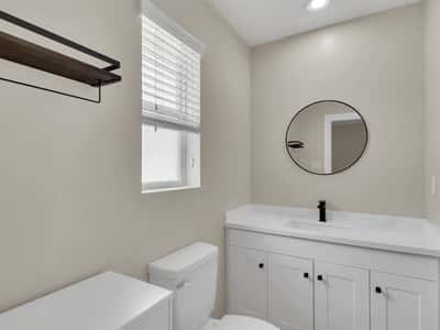 Modern bathroom featuring a quartz vanity, contemporary cabinetry, matte black faucet, and stylish round mirror. Updated finishes create a clean, inviting space in this Phoenix rental.