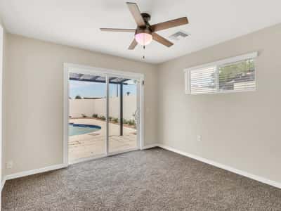 Spacious bedroom with sliding glass doors leading directly to the backyard and pool area, plush carpeting, and a ceiling fan. Enjoy private indoor-outdoor living in this remodeled Phoenix rental.