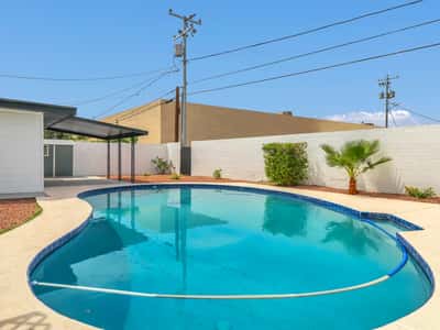Spacious backyard featuring a refreshing swimming pool, covered patio, mature landscaping, and low-maintenance grounds. Enjoy comfortable outdoor living at this beautifully updated Phoenix rental.