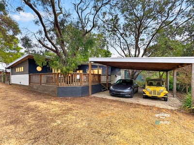 This unique property features a spacious deck and ample parking under a sheltered carport, surrounded by lush greenery.