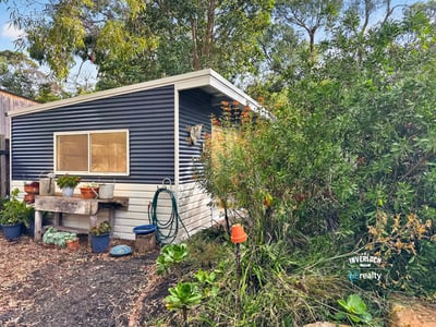 Quaint cottage nestled among lush greenery, offering a unique retreat with potential for creative landscaping.