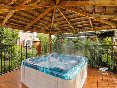 Relax in this private hot tub surrounded by lush landscaping under a rustic wooden pergola.