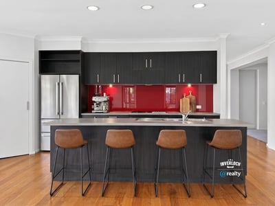 Modern kitchen featuring sleek cabinetry, a striking red backsplash, and spacious island with bar seating.