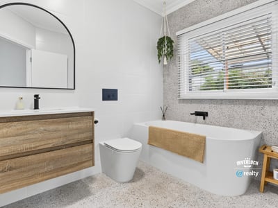 Modern bathroom featuring a freestanding tub, large mirror, and ample natural light from the window.