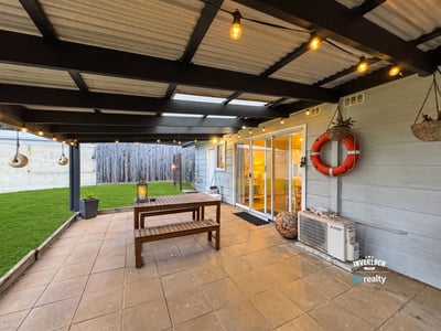 Spacious outdoor patio with hanging lights and lawn, perfect for gatherings and relaxed evenings.