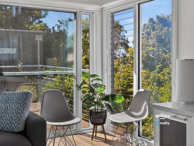 Bright and airy living space featuring large windows and a balcony with lush outdoor views.