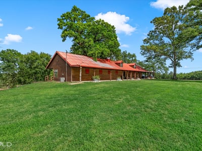 Spacious countryside home with a welcoming porch, surrounded by lush greenery and open skies.