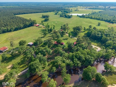 Expansive acreage with lush landscapes, multiple structures, and serene water features ideal for various outdoor endeavors.