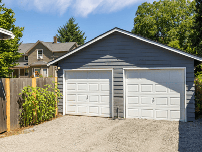 This spacious two-car garage features ample storage and easy access from a gravel driveway.