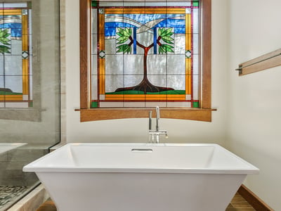 Relaxing soaking tub framed by decorative stained glass and warm wood trim. This peaceful bathroom retreat blends artistry with luxury finishes.