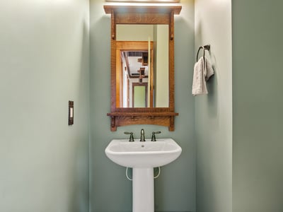 Designer half bath with pedestal sink, custom mirror, and handcrafted wood accents. A polished space that adds charm and convenience for visitors.