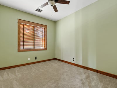 Featuring green walls, soft carpeting, and a ceiling fan, this secondary bedroom offers comfort and charm in a tranquil corner of the house.